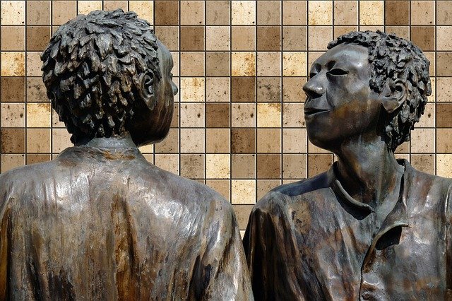 Photo of a sculpture showing the heads of two people talking to each other.